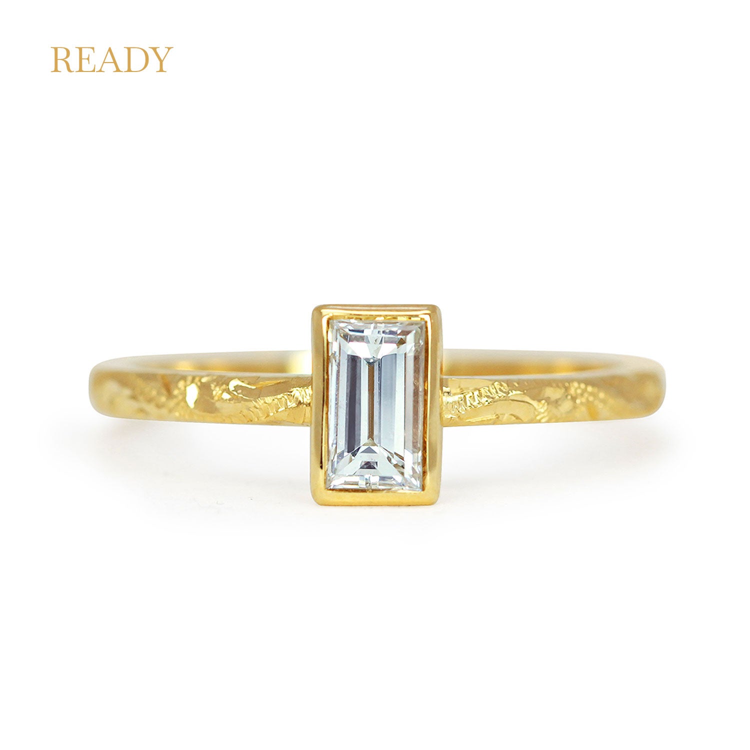 Lebrusan Studio Fancy Hera ready to wear engagement ring with a recycled baguette solitaire diamond in a rub-over setting; an 18ct recycled gold band is hand engraved with scrolls