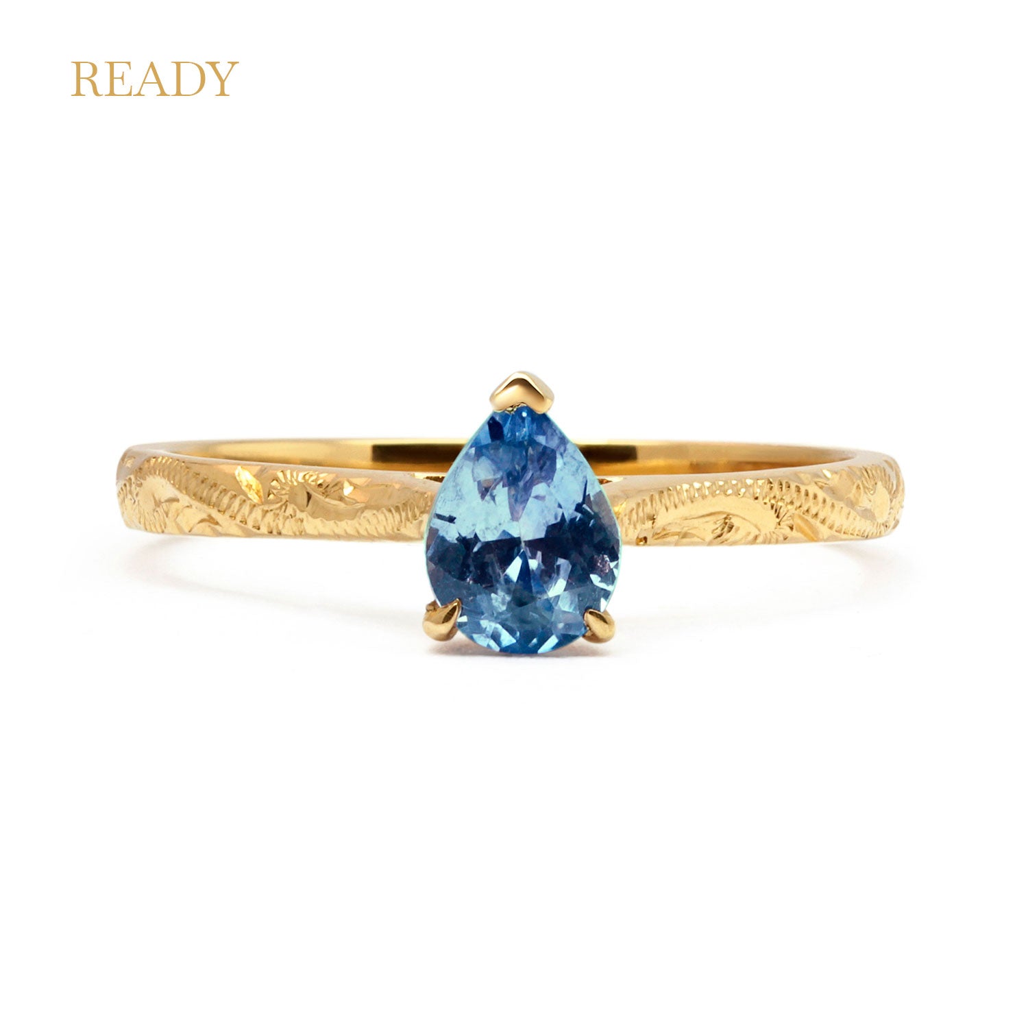 Fancy Athena ethical solitaire engagement ring in 18ct yellow artisanal Fairmined Ecological Gold, hand-engraved and set with a blue pear-cut sapphire of fair-traded and traceable Sri Lankan provenance