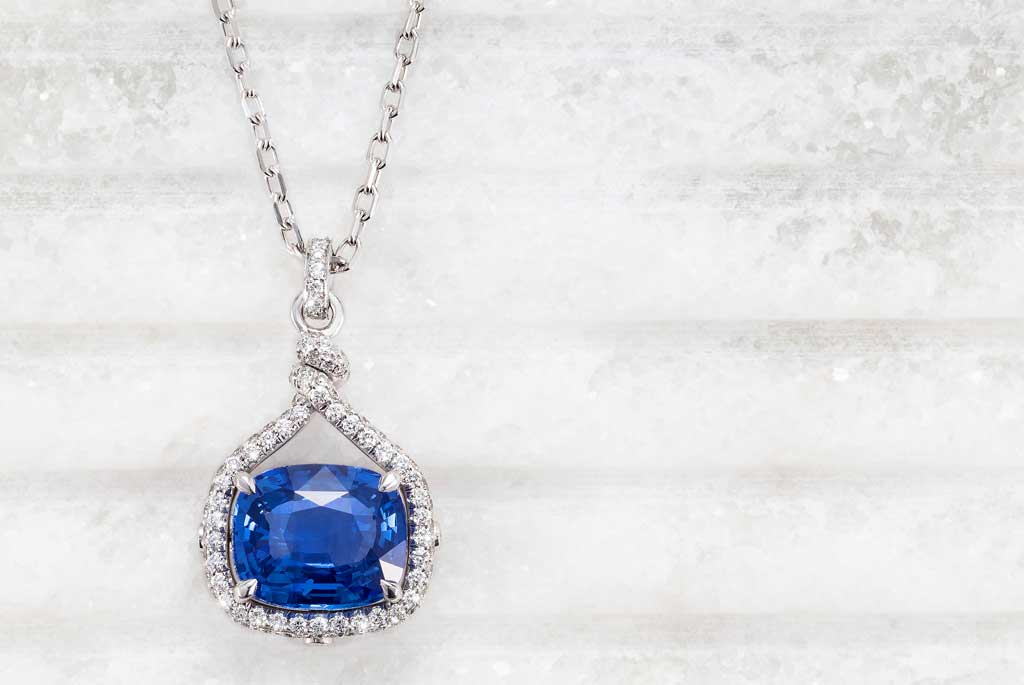 Bespoke white gold necklace with a fair-traded blue cushion-cut sapphire and a halo of ethically sourced diamonds