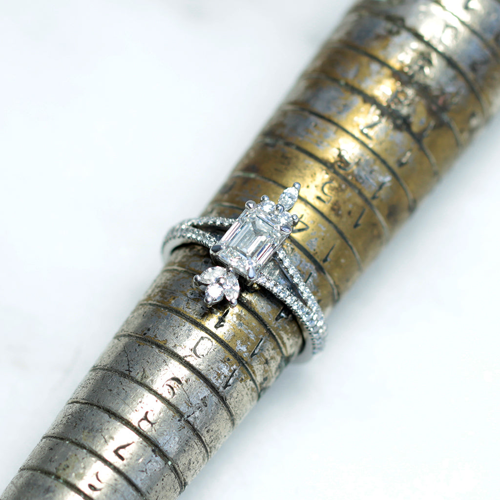 A bespoke engagement ring set with a vertical emerald-cut Canadamark diamond, two fans of conflict-free marquise-cut diamonds either end and a split band microset with more conflict-free diamonds, sitting on a vintage-style ring sizing rod