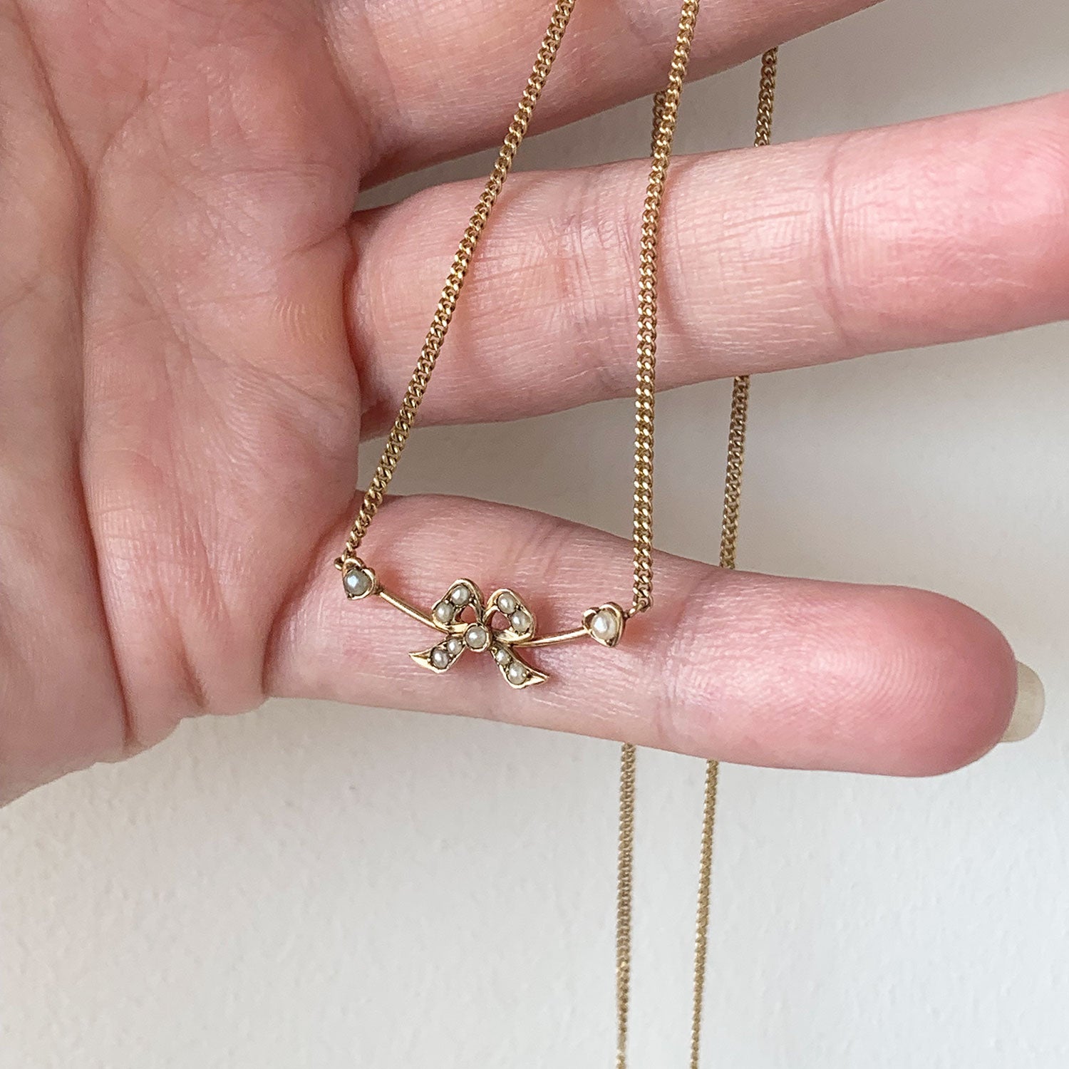 Gold necklace with white pearls in the shape held by a hand on a white background