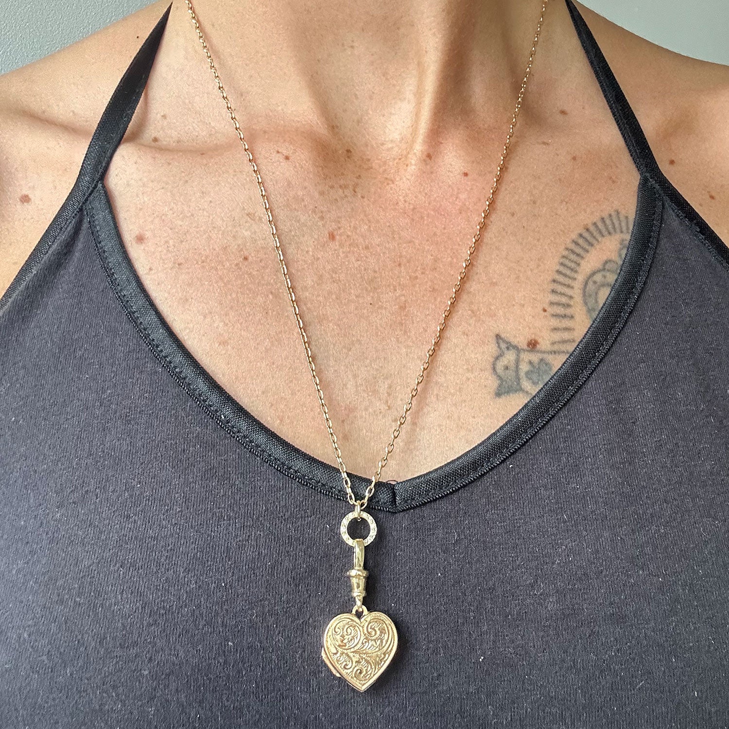 Reclaimed antique Victorian hand-engraved gold heart-shaped locket pendant necklace on a reclaimed antique gold chain, with a circlet connector in sustainable recycled gold and conflict-free Canadian diamonds, modelled on body