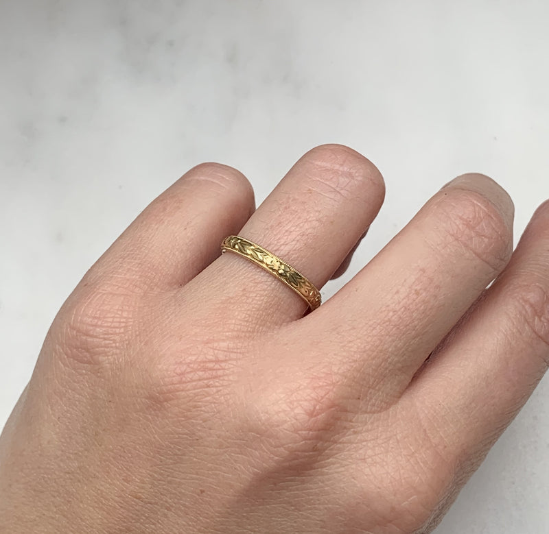A D-shaped 2mm wedding band in 18ct recycled yellow gold, carefully hand-engraved with a repetitive orange blossom motif and a border of milgrain beading