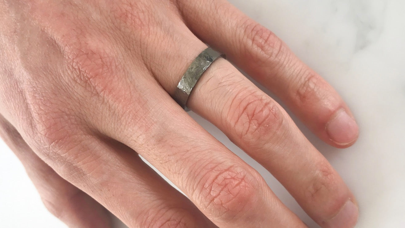 A flat men's wedding band finished with black rhodium plating and hard hammering