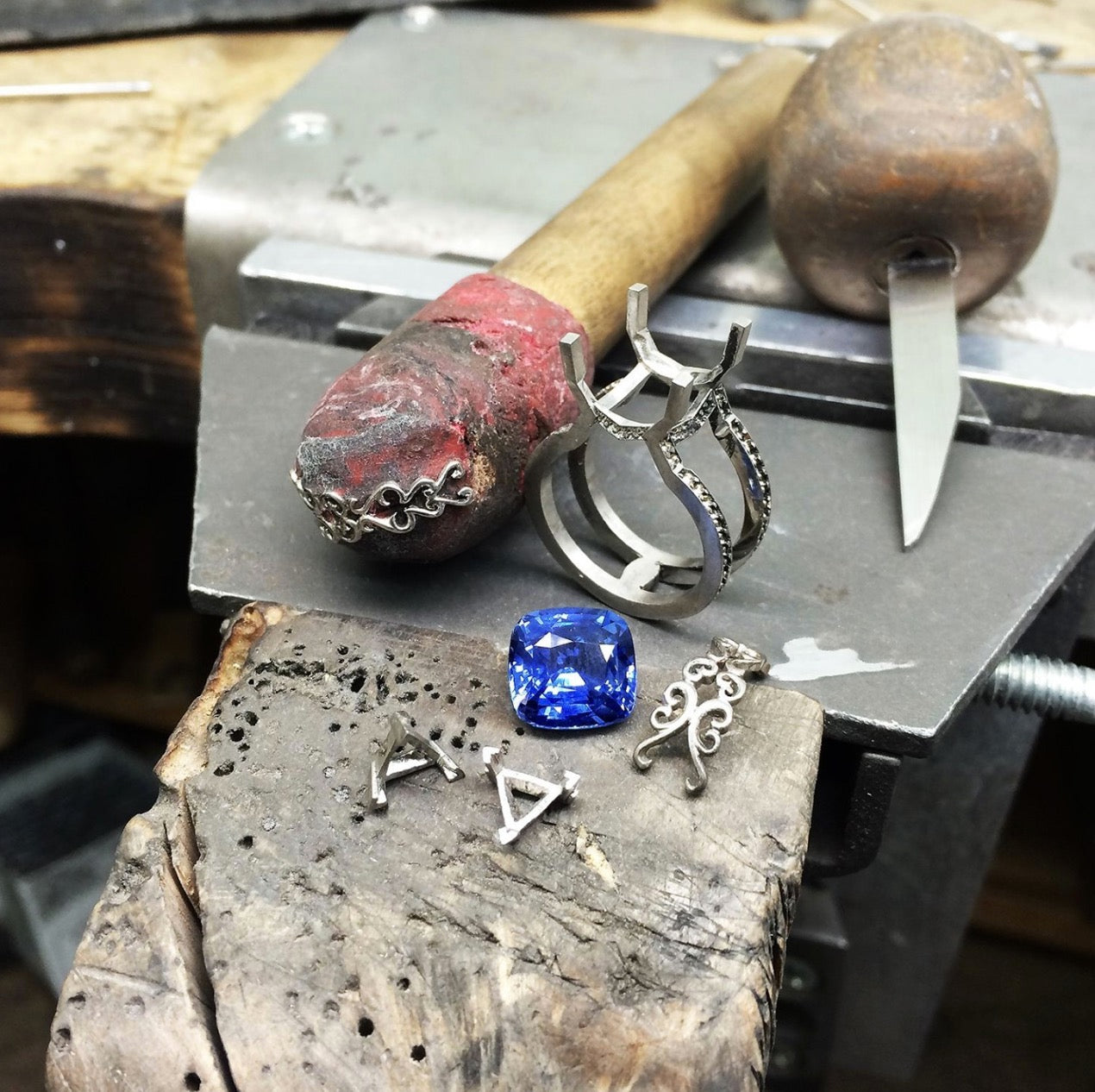 The components of a bespoke cocktail ring sit on a London jewellery makers manufacturing bench. Ethical gold settings and detailing will eventually play host to a 7.05ct cushion-cut traceable and fair-traded blue sapphire. Ring designer London.