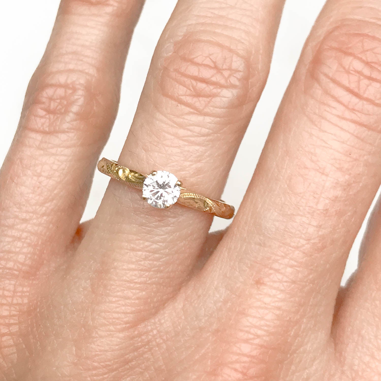 Solitaire engagement ring with a slim 18ct yellow gold band hand-engraved with intricate scrolls, and a 0.33ct round brilliant-cut diamond in a traditional four-claw setting, on hand