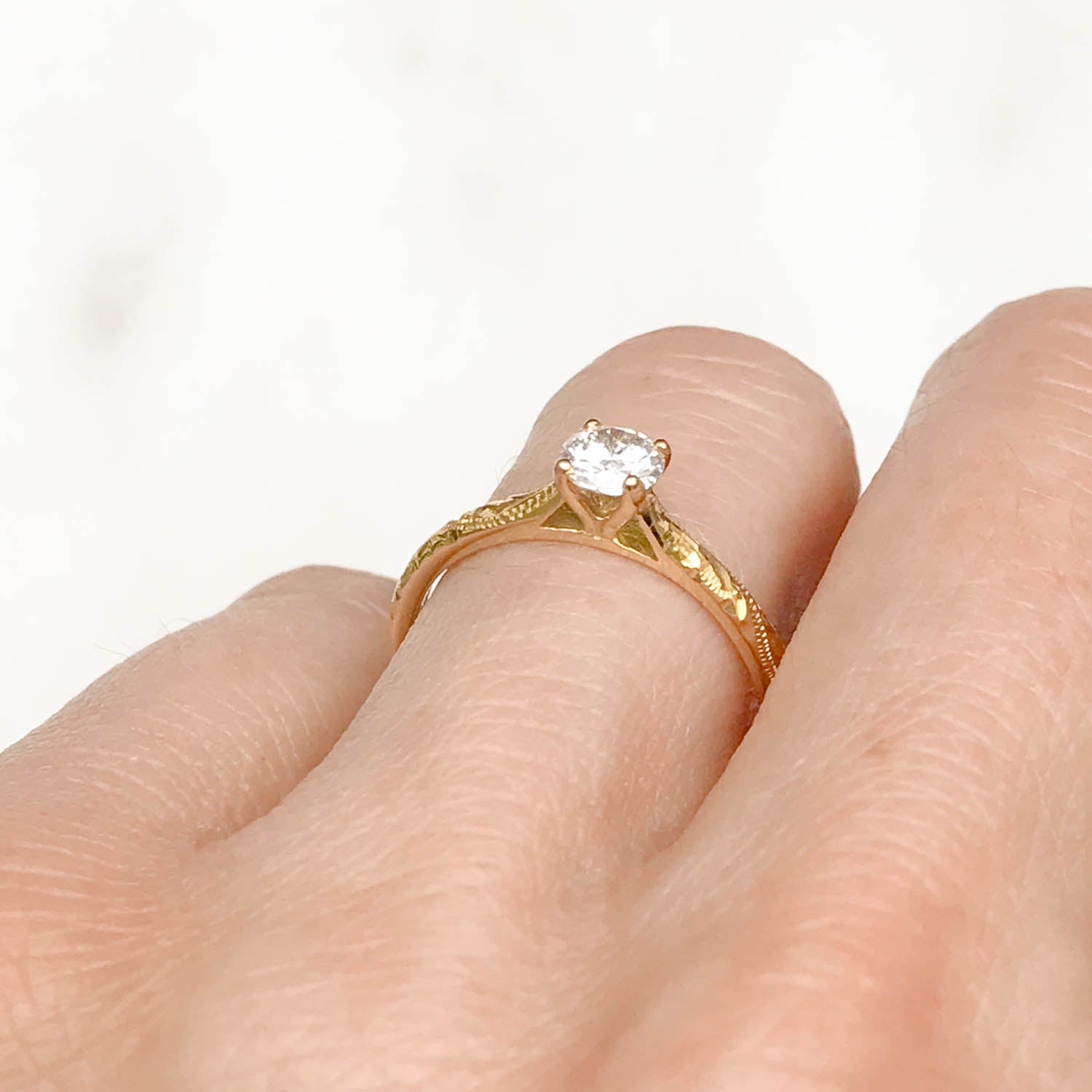 Solitaire engagement ring with a slim 18ct yellow gold band hand-engraved with intricate scrolls, and a 0.33ct round brilliant-cut diamond in a traditional four-claw setting, on hand, POV