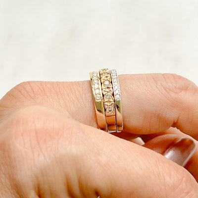 Three antique 9ct gold Victorian eternity rings half-set with diamonds, soldered together into a chunky stack, side view to show contrasting setting styles, on hand