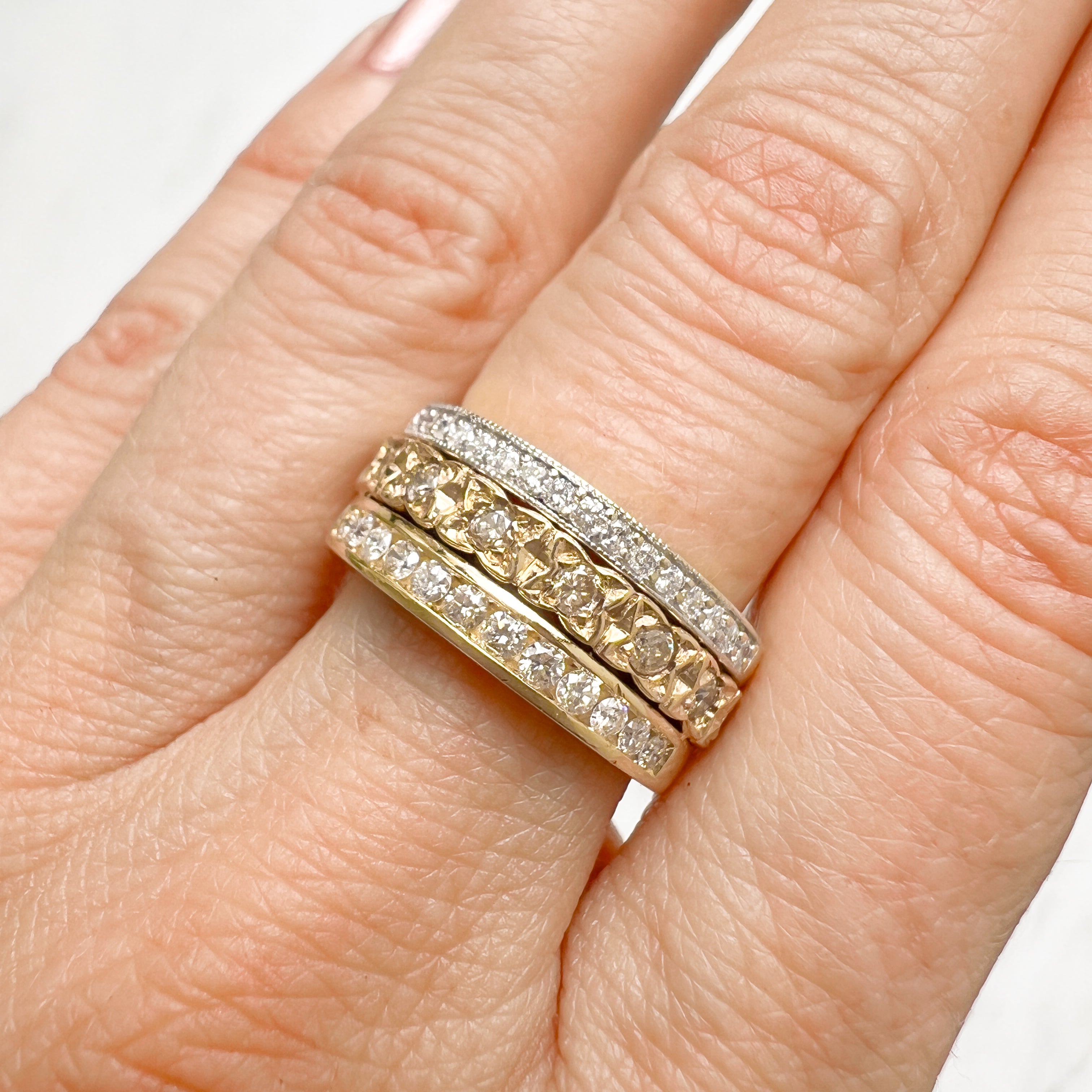 Three antique 9ct gold Victorian eternity rings half-set with diamonds, soldered together into a chunky stack, on hand