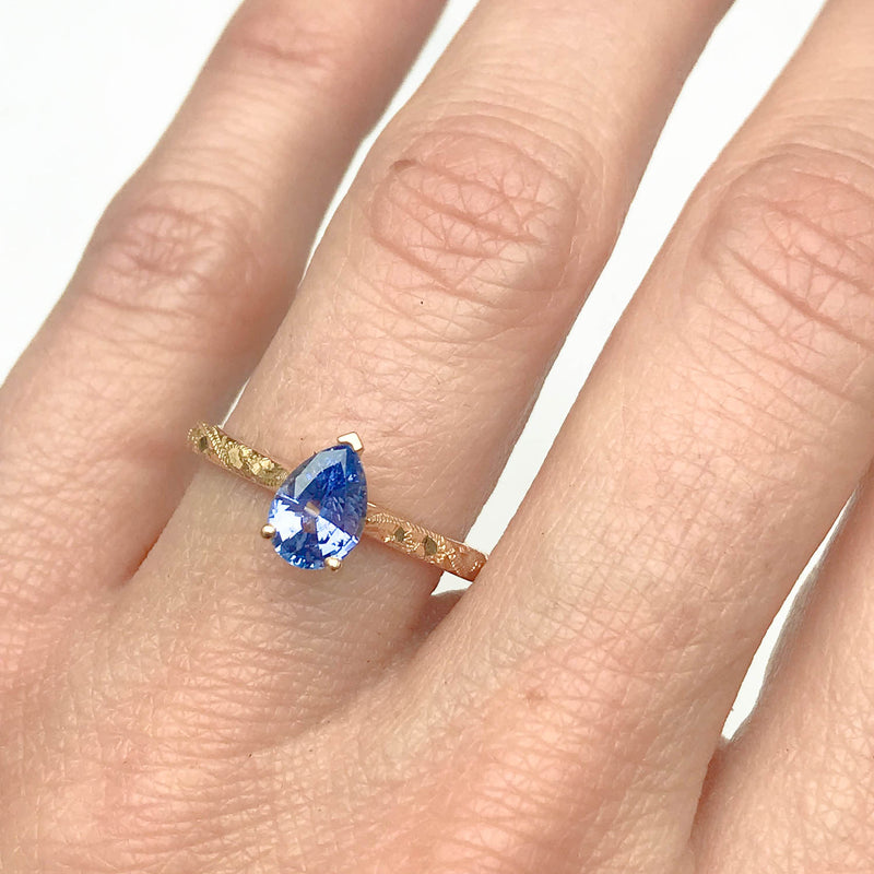 Fancy Athena ethical solitaire engagement ring in 18ct yellow artisanal Fairmined Ecological Gold, hand-engraved and set with a blue pear-cut sapphire of fair-traded and traceable Sri Lankan provenance