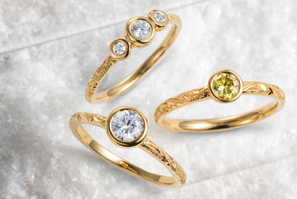 Trilogy and solitaire engagement rings from Hera, Lebrusan Studio's collection of contemporary engagement rings. The pieces are characterised by slim hand-engraved yellow gold bands and conflict-free yellow and white diamonds in rub-over settings