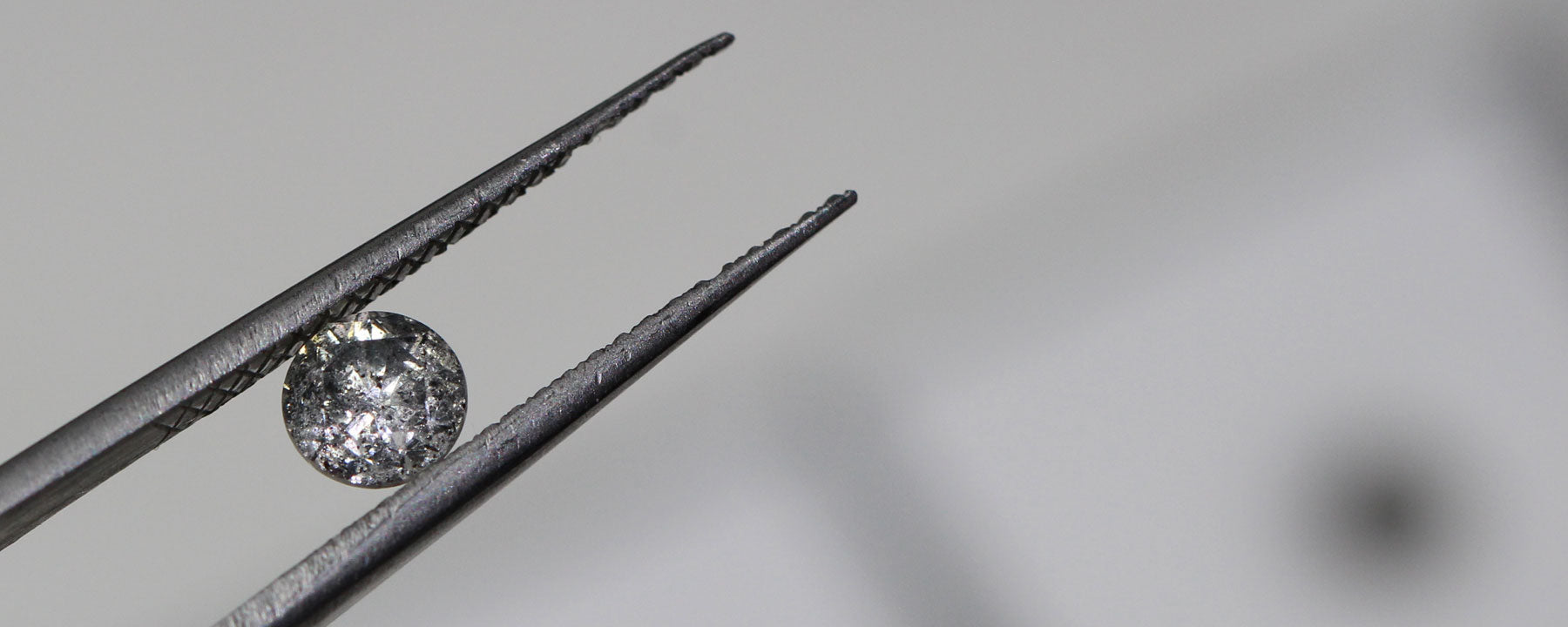 Tweezers holding a brilliant-cut salt and pepper diamond