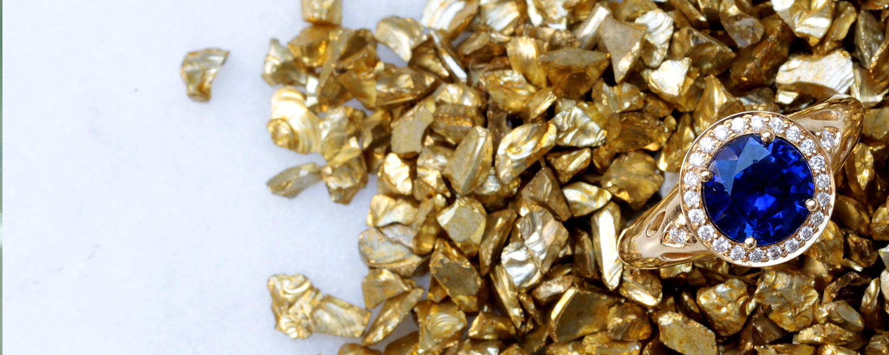 A bespoke sapphire and diamond engagement ring. Centre-stage is a large round blue sapphire of traceable and fair-traded origin, enveloped in a halo of conflict-free diamonds. The band is chunky and cast in yellow ethical gold. London designer jewellery