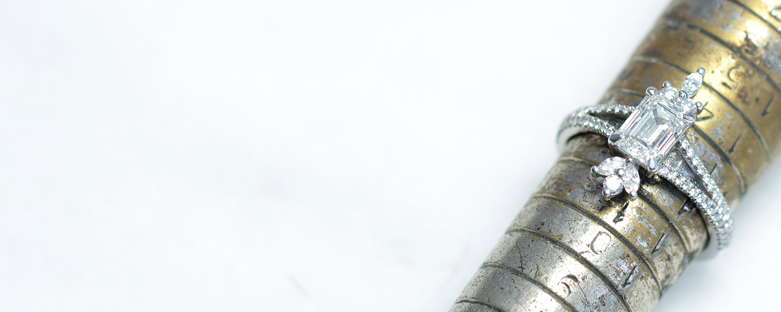 A Lebrusan Studio custom made engagement ring, slotted onto a traditional ring sizing rod. The jewel, crafted by London jewellery makers in Hatton Garden, is cast in 18ct white recycled gold and set with a large emerald-cut Canadian diamond.