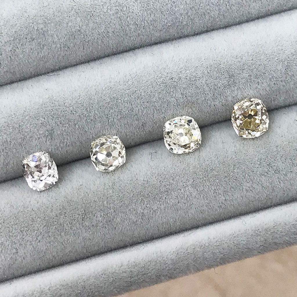 Four vintage recycled old cushion-cut diamonds, lined up on a gemstone cushion waiting to be set into ethical bespoke jewellery by London jewellery makers