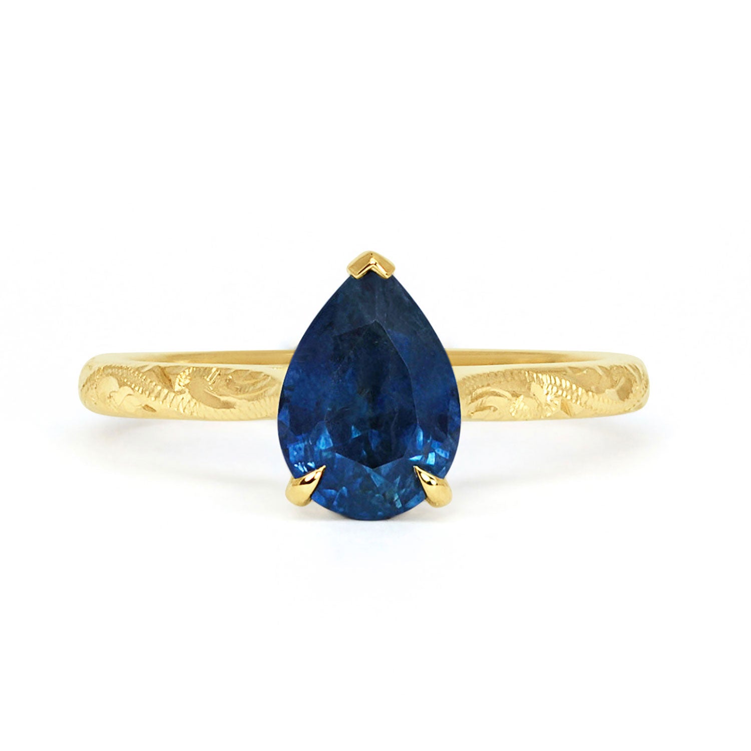 Solitaire engagement ring with a large pear-cut blue sapphire secured in a classic claw solitaire setting. 18ct recycled gold is hand engraved with scrolls