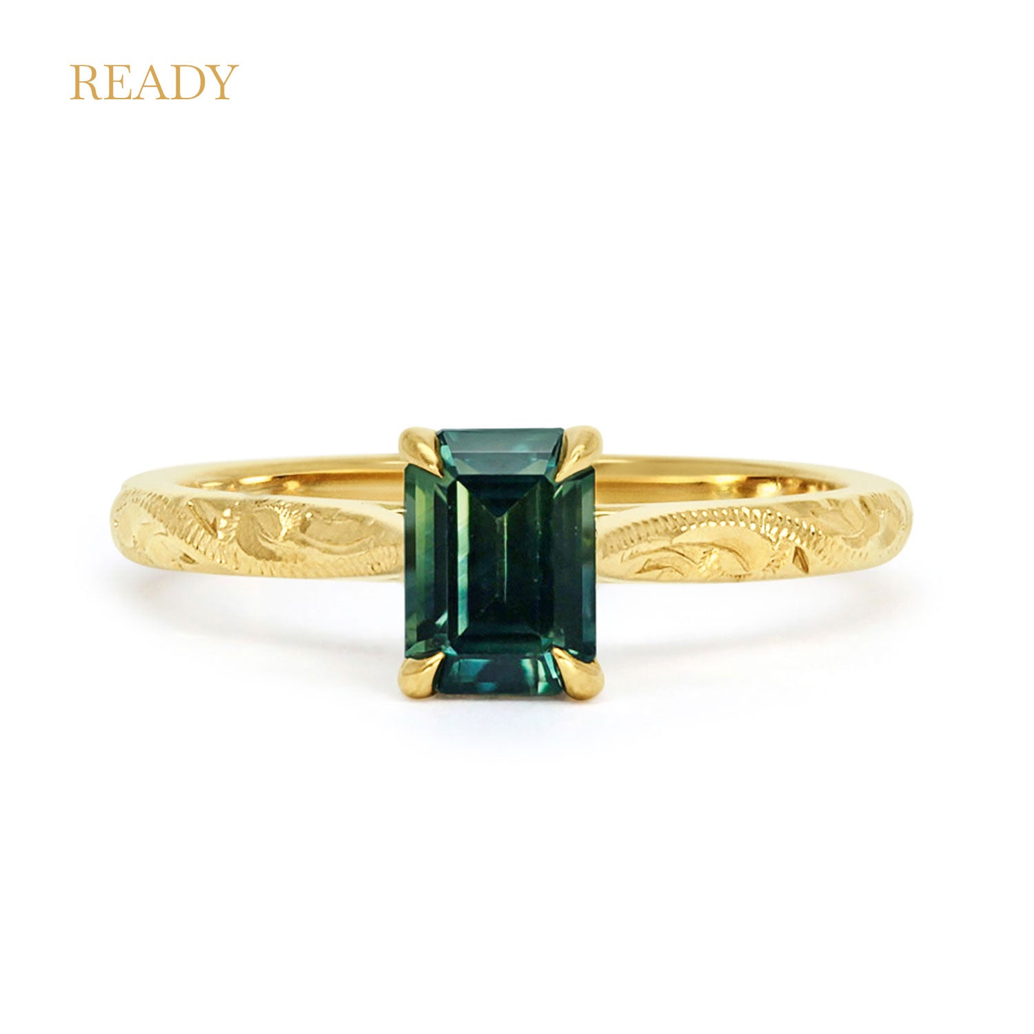 18ct recycled gold solitaire engagement ring with a baguette teal sapphire in a classic solitaire claw setting and a hand engraved band