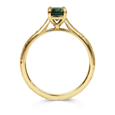18ct recycled gold solitaire engagement ring with a baguette teal sapphire in a classic solitaire claw setting and a hand engraved band, side view