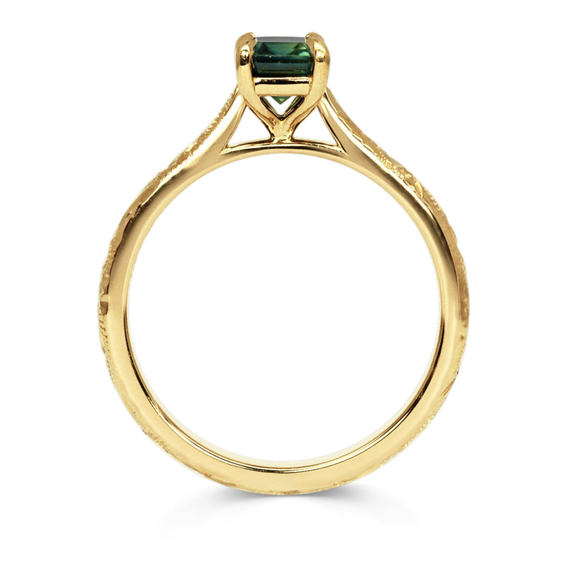 18ct recycled gold solitaire engagement ring with a baguette teal sapphire in a classic solitaire claw setting and a hand engraved band