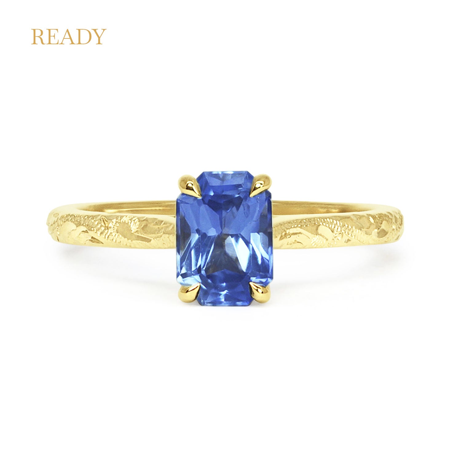 Lebrusan Studio Athena solitaire engagement ring with a hand-engraved 18ct yellow gold band and an emerald-cut blue sapphire 