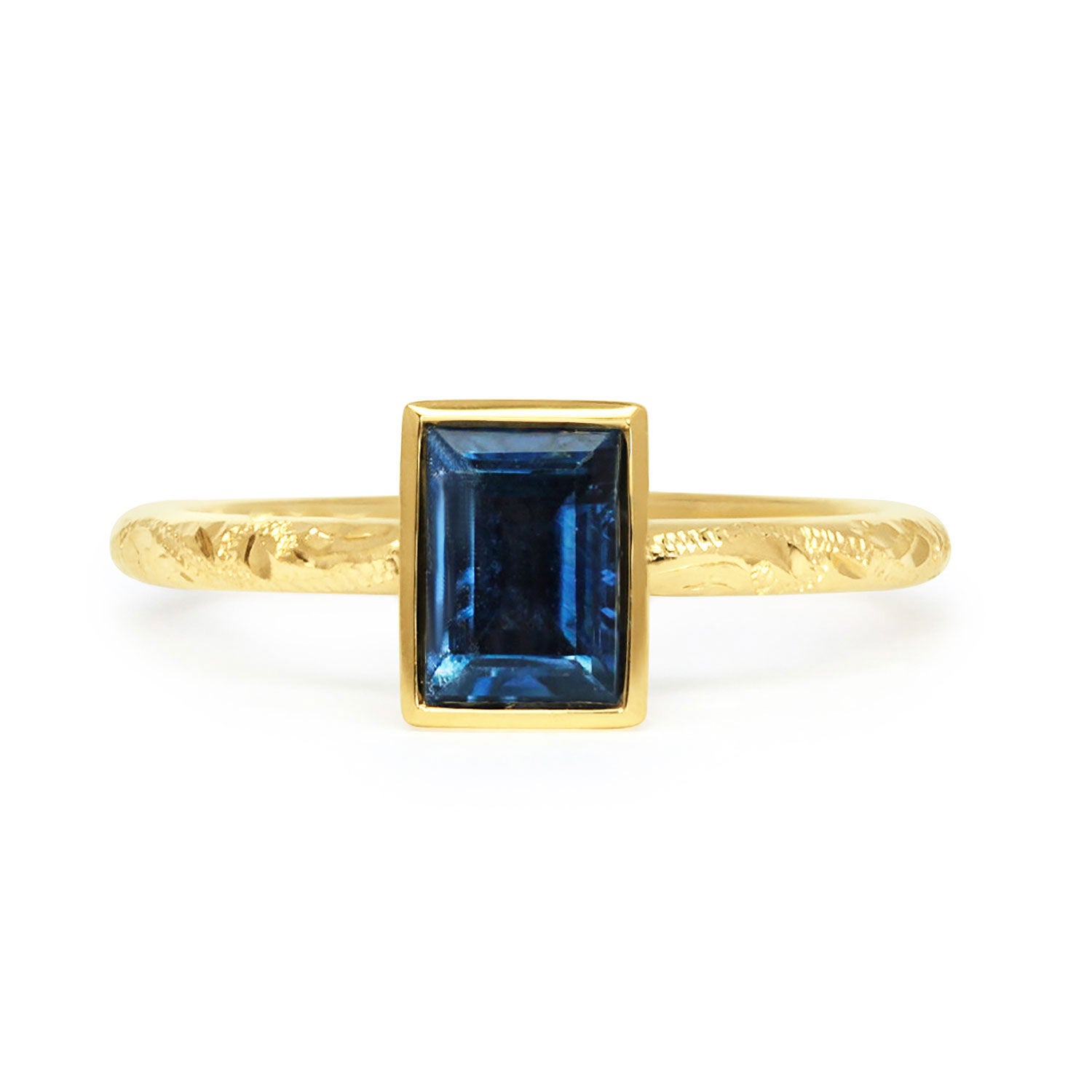 Solitaire engagement ring with a baguette-cut deep blue sapphire, secured in an 18ct recycled gold rub-over setting and a band hand-engraved with scrolls