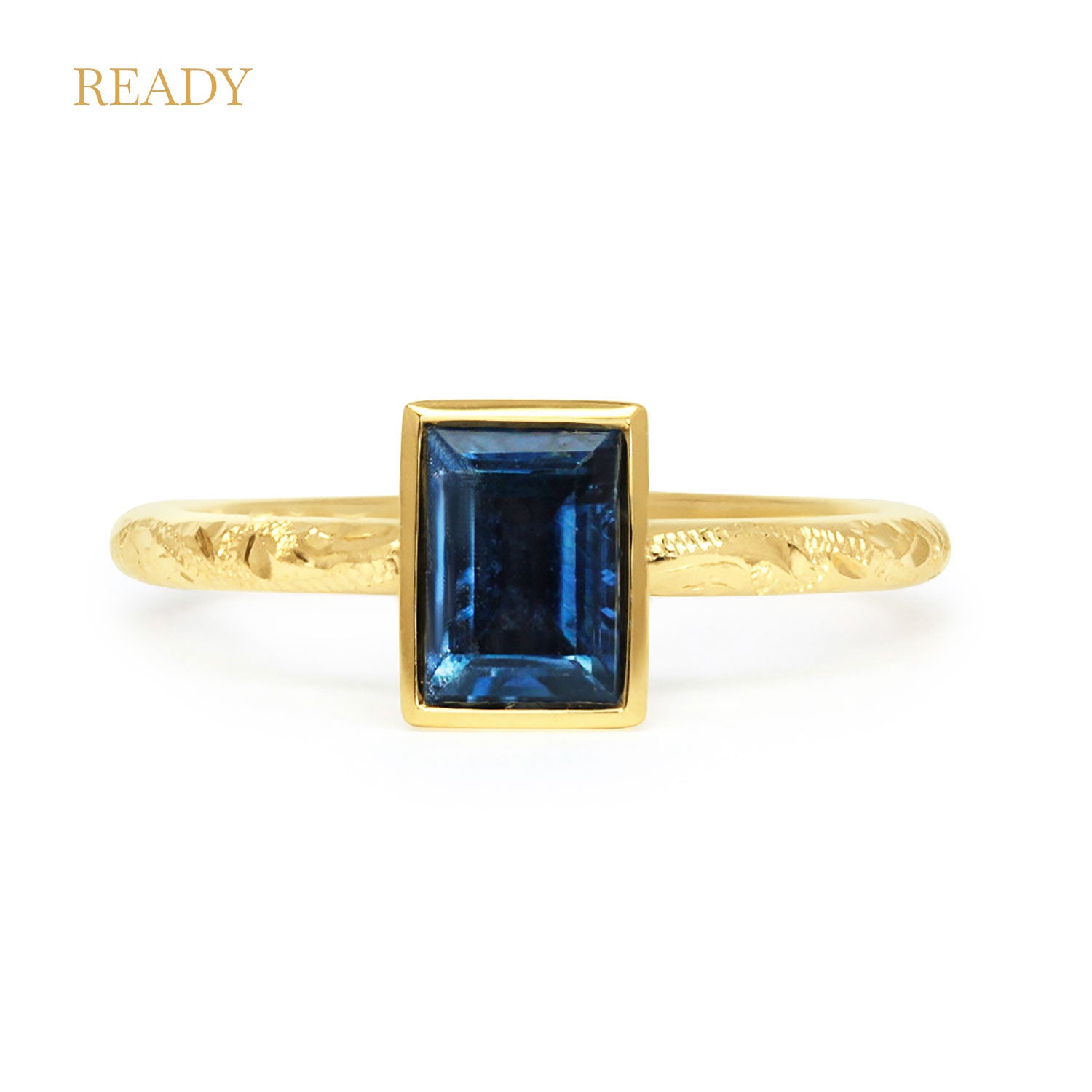 Solitaire engagement ring with a baguette-cut deep blue sapphire, secured in an 18ct recycled gold rub-over setting and a band hand-engraved with scrolls