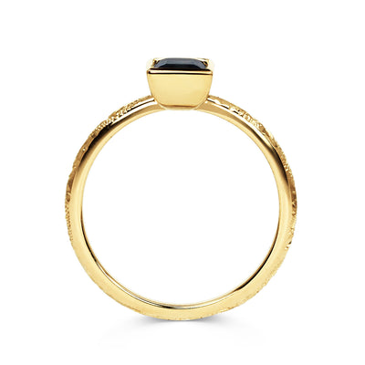 Solitaire engagement ring with a baguette-cut deep blue sapphire, secured in an 18ct recycled gold rub-over setting and a band hand-engraved with scrolls, side view