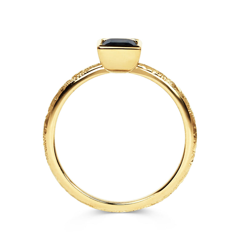 Solitaire engagement ring with a baguette-cut deep blue sapphire, secured in an 18ct recycled gold rub-over setting and a band hand-engraved with scrolls