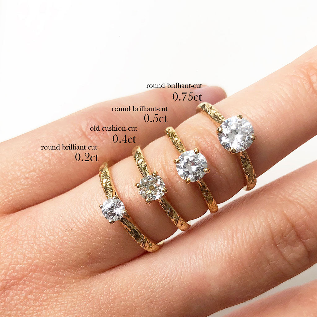 Four Lebrusan Studio Athena engagement rings lined up alongside one another, set with ethical and conflict-free diamonds of varying sizes. The bands are delicate, cast in recycled yellow gold and hand-engraved. Simple but unique engagement rings