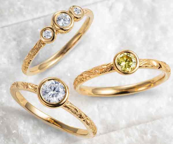 Three ethical engagement rings from the Hera collection, characterised by lab-grown diamonds, recycled gold, hand-engraved bands and rub-over gemstone settings