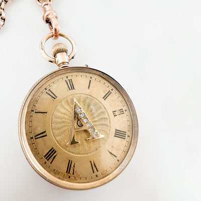 Reclaimed Vintage antique Victotrian pocket watch with Roman numerals and a decorative 'A', set with broken diamonds - repurposed as a pendant on a reclaimed antique gold chain and Albert clasp - on a white background