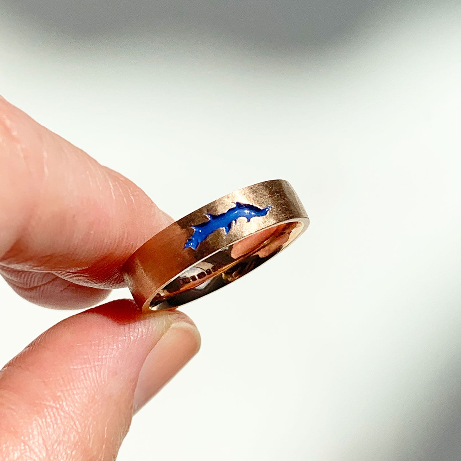 Bespoke flat court wedding band, finished with soft hammered and matte texture and a fissure inlayed with blue enamel. 9ct recycled rose gold reworked from an old heirloom piece. In the sunshine