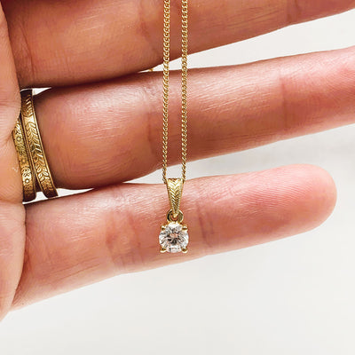 Lebrusan Studio's ethical Perfectus pendant necklace, crafted in London, UK, using 18ct Fairtrade Gold and a recycled diamond. A hand-engraved floral motif and proud claw setting are finishing touches. Lifestyle shot dangling in a model's hand