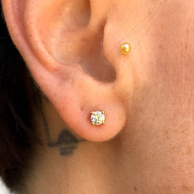 Lebrusan Studio rub-over stud earrings with milgrain beading - 18ct yellow Fairtrade Gold and 0.5ct of recycled diamonds, lifestyle photo on ear 2