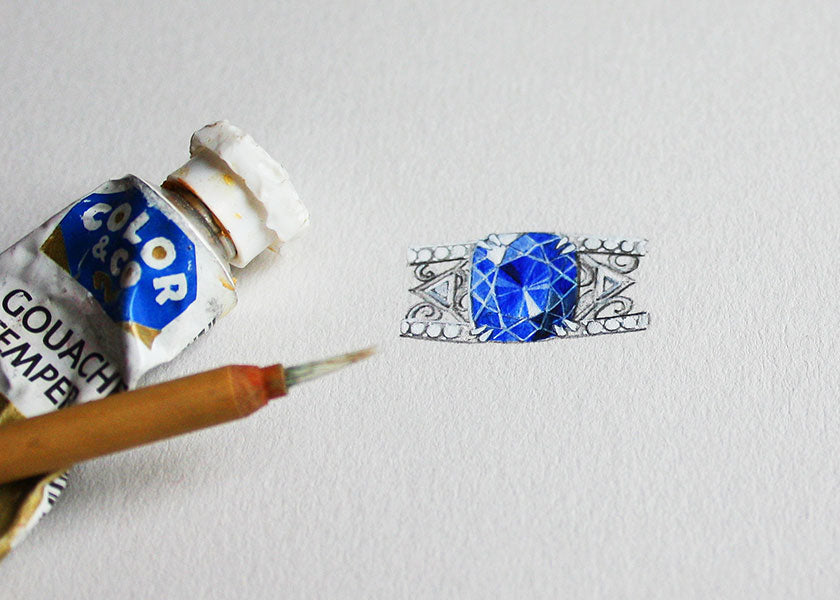 A hand-painted bespoke design of a large sapphire-set engagement ring, on paper alongside a paintbrush and a tube of oil paint