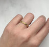 A D-shaped 2mm wedding band in 18ct recycled yellow gold, carefully hand-engraved with a repetitive orange blossom motif and a border of milgrain beading, on the ring finger of the left hand