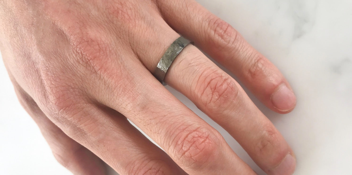 A flat men's wedding band finished with black rhodium plating and hard hammering