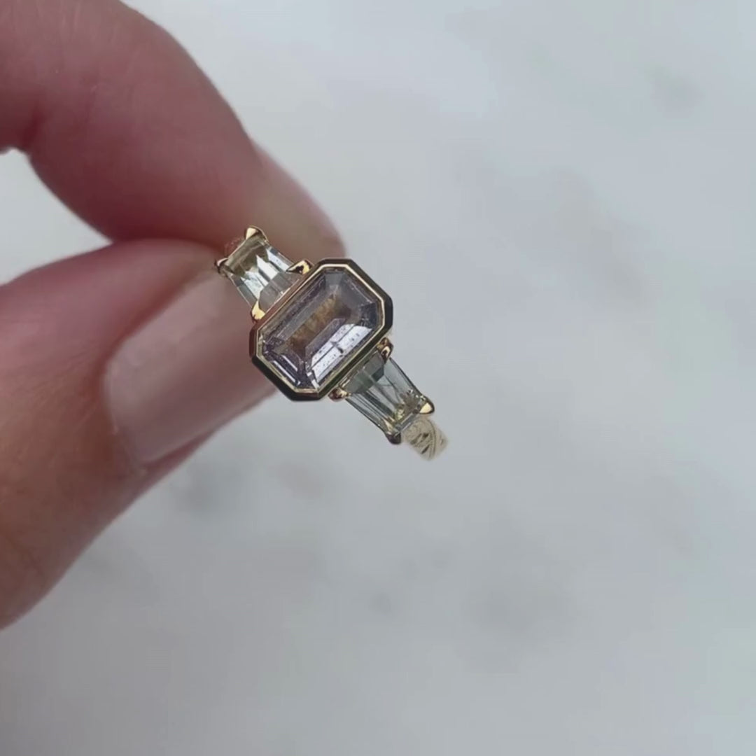 Lebrusan Studio Fancy Athena trilogy engagement ring with hand-engraved 18ct yellow Fairmined Eco Gold band and three emerald cut grey sapphires of ethical traceable origin, video