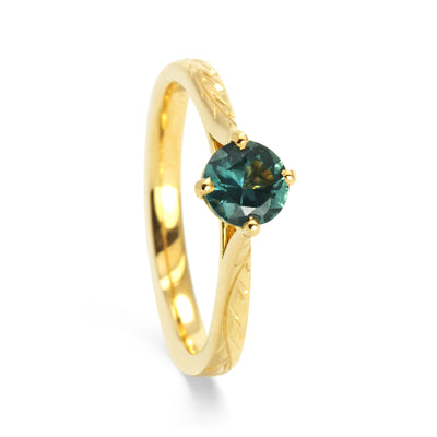 Bespoke Ed nature-inspired solitaire engagement ring, 18ct recycled yellow gold, hand-engraved fines and a traceable teal sapphire from Montana side