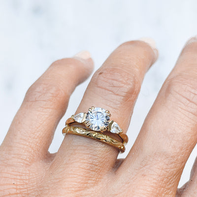 Lebrusan Studio Artisan Trilogy Engagement Ring, 1ct Ocean Diamond, 0.3ct pear-cut side Ocean Diamonds, 18ct Fairmined Ecological Gold, hand engraving, on hand, along with our hand-engraved Scrolls Ethical Gold Wedding Ring